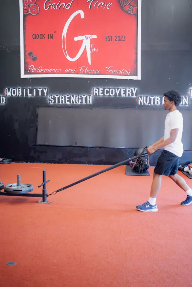 Athlete pulling a sled under the Grind Time Clock In sign